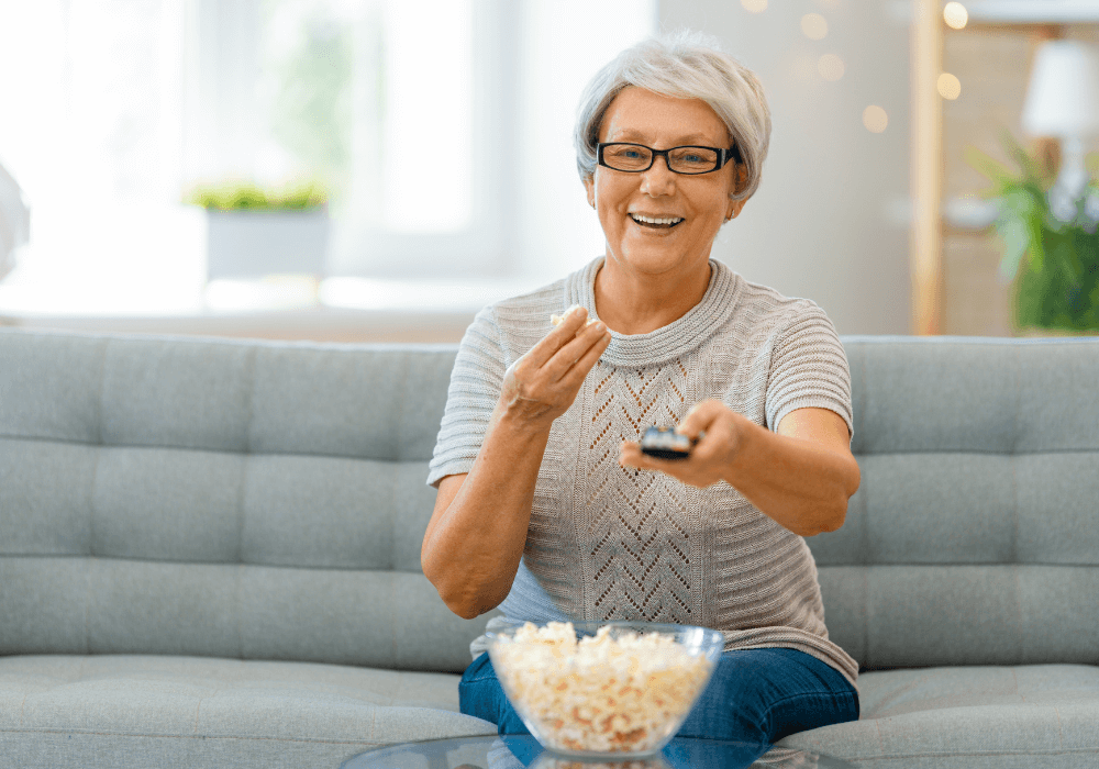 senior woman eating popcorn while holding remote best tv remote for seniors