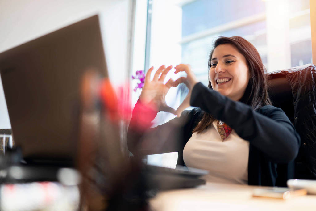 女人在办公室视频聊天，同时用她的手做心形
