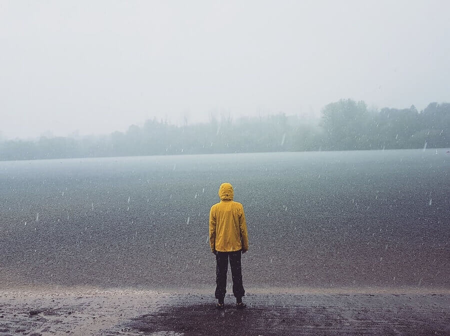 站立在雨中的湖的人雨包装的雨夹克男人