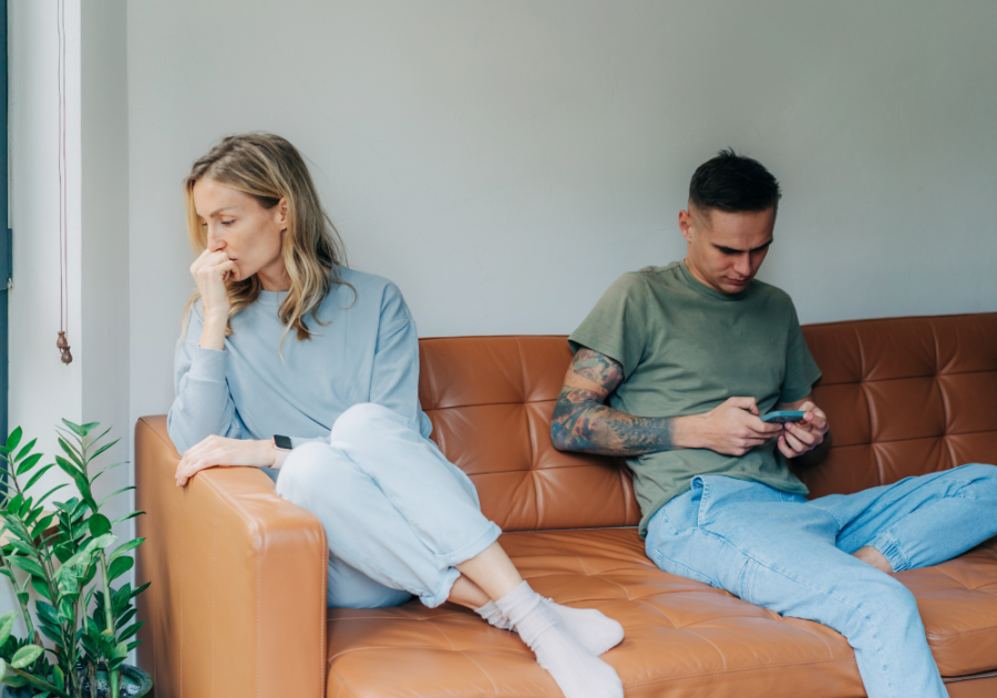 man sitting in couch using phone while woman is sitting far away signs he wants you to leave him alone