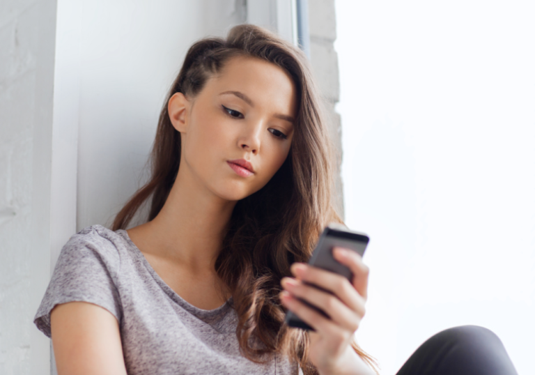woman sitting by the window looking at phone