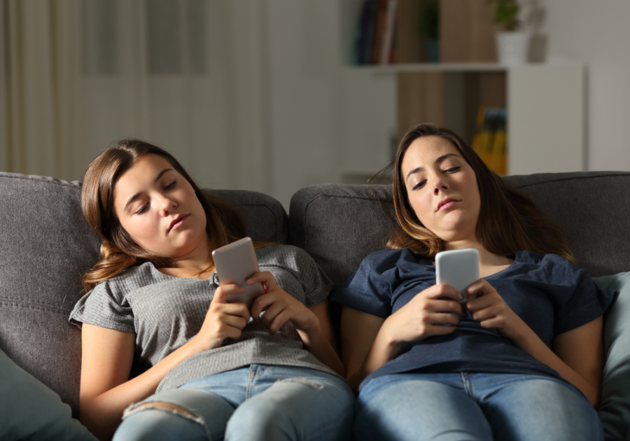 两个女孩在沙发上放松，一边看手机，一边停止联系朋友