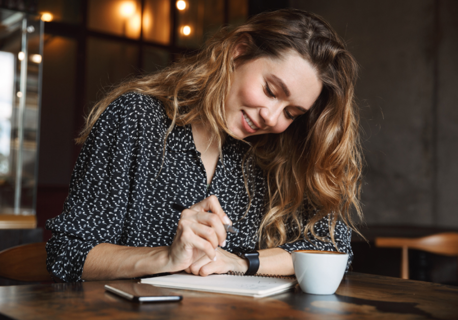woman smiling while writing in her notebook anniversary messages to your boyfriend