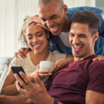 group sitting behind man with phone smiling 251 Best Paranoia Questions Game To Play With Friends