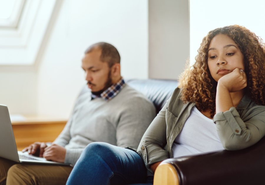 couple sitting on sofa man is looking on laptop woman is sad Signs of Emotional Neglect in a Marriage