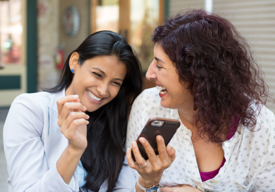 women laughing looking at phone Funny Jokes To Tell Your Friends