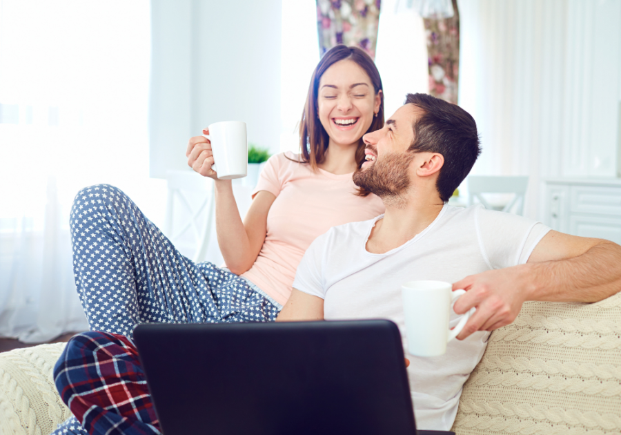 couple sitting on sofa laughing Funny Questions For Couples