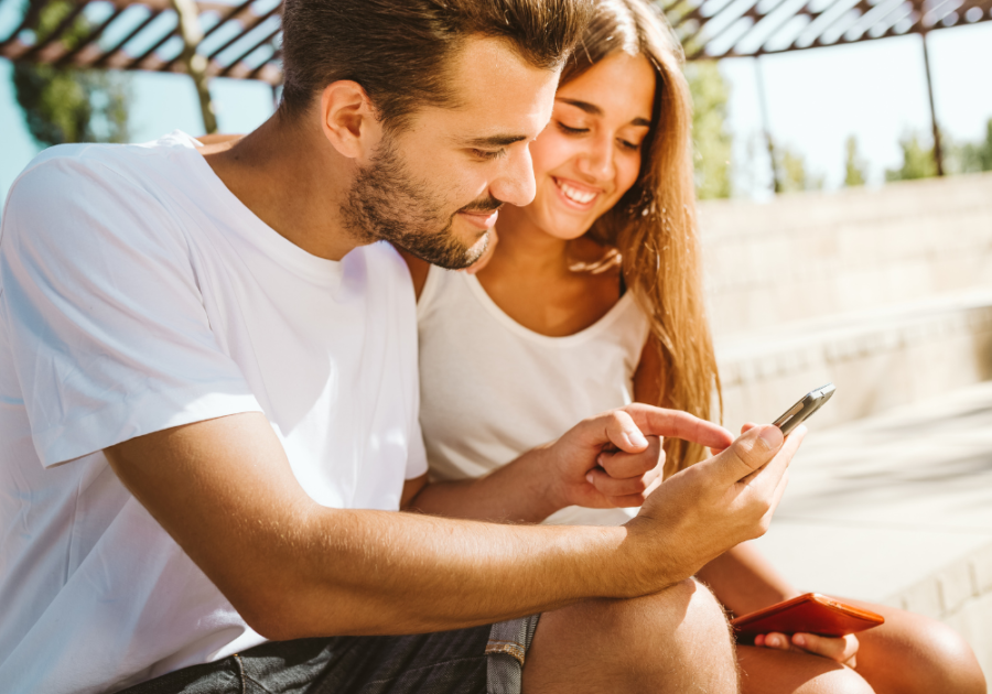 couple outdoors looking at phone smiling Would You Rather Questions for Couples