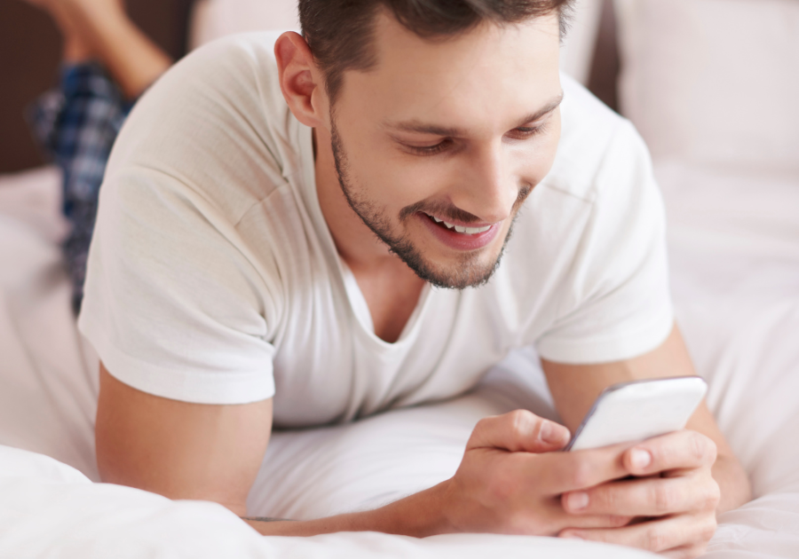 man laying on bed smiling at phone Interesting Questions to Ask a Girl Over Text 