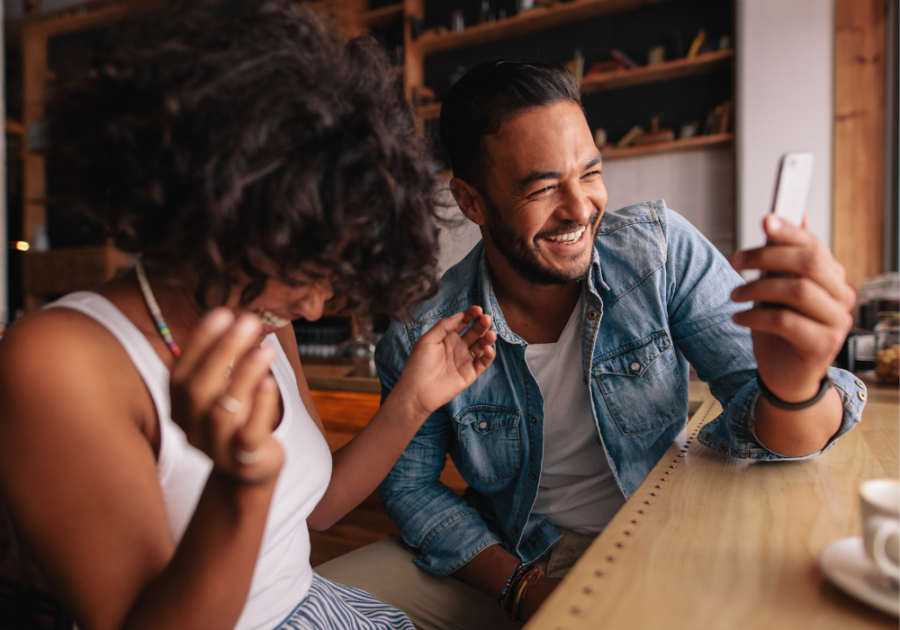 couple laughing looking at phone Would You Rather Questions for Couples