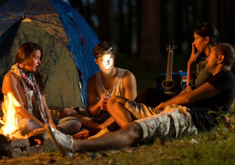 friends camping sitting by fire at night scary games to play with friends