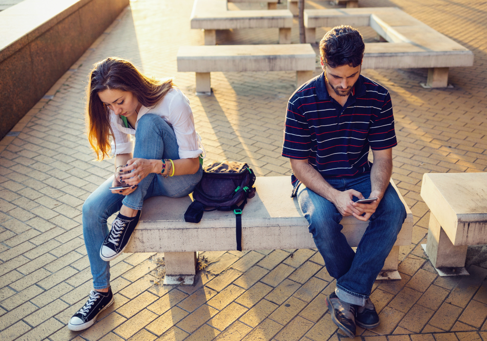 young man and woman sitting far from each other while using phone signs the relationship is over for him
