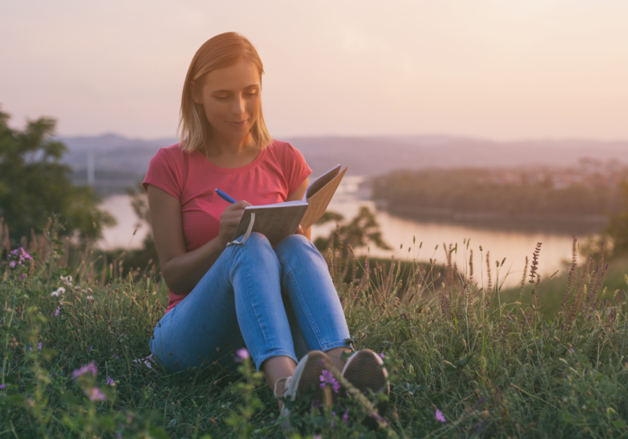 woman writing down in her notebook while sitting in the field open when letters for him