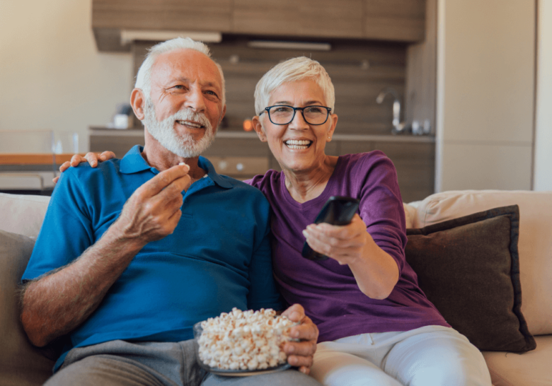 高级女性持有remote while husband is holding popcorn best movies for seniors